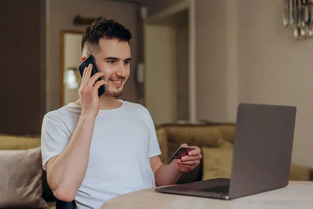 Persona feliz usando su celular y laptop para solicitar un prestamo en linea