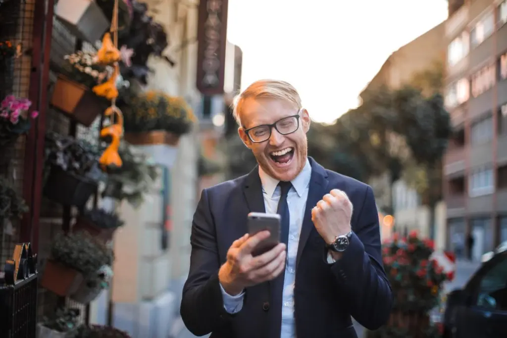 Hombre celebrando una buena noticia financiera en su telefono