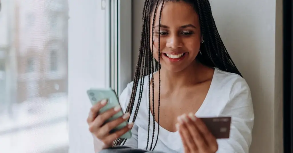 Mujer sonriente usando su celular y tarjeta para compra en línea