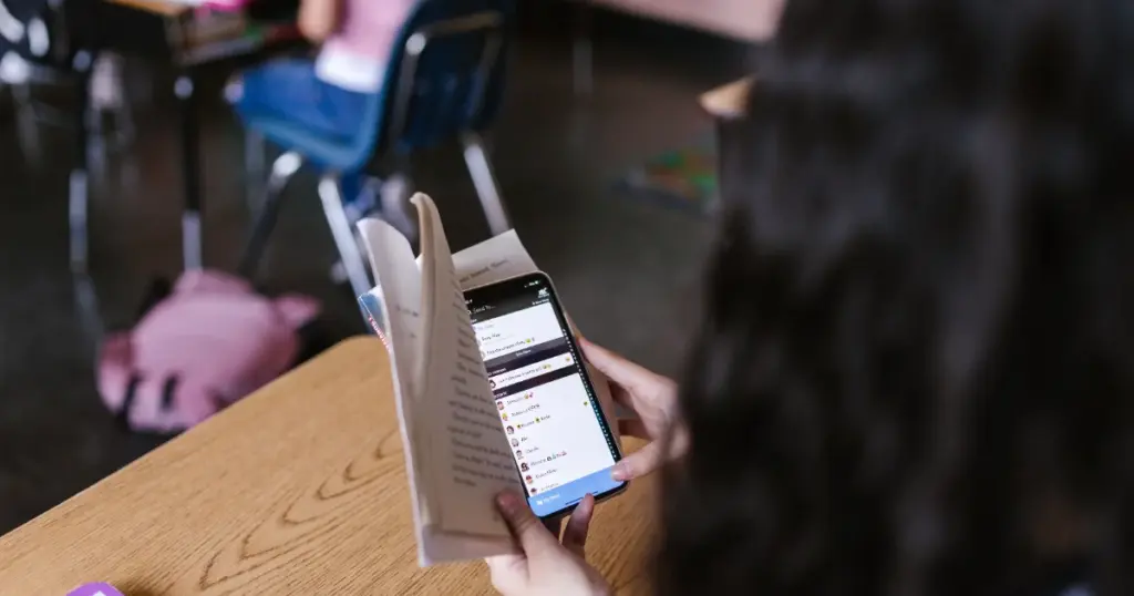 Joven estudiante revisando su celular con libros