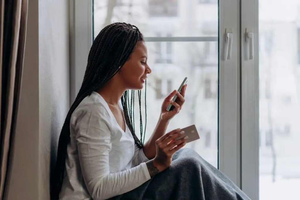 Mujer revisando en su celular una transferencia mientras sostiene una tarjeta