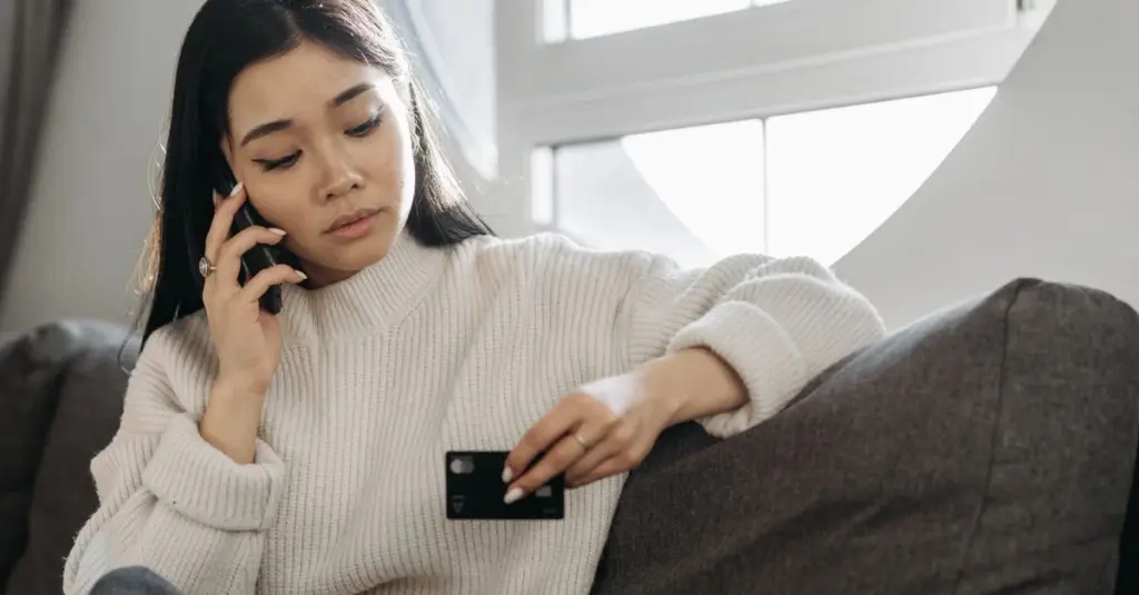 Mujer revisando su tarjeta y su celular en casa
