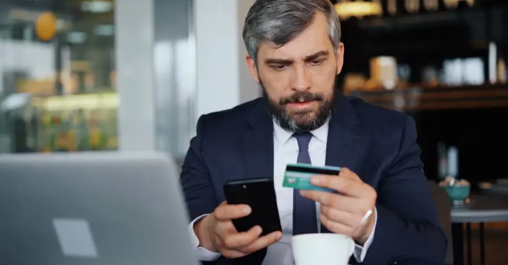 Hombre de traje usando celular y tarjeta en un cafe