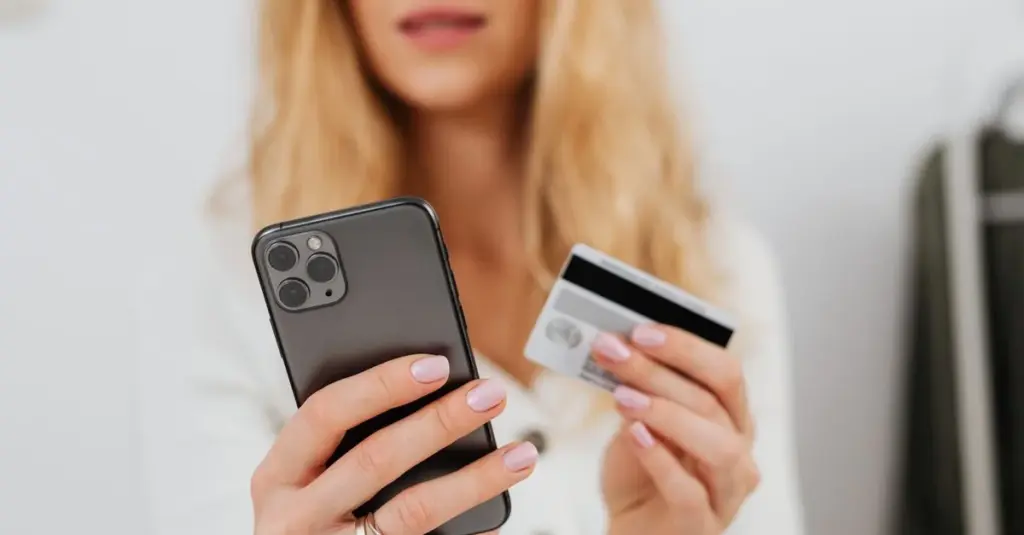 Mujer usando tarjeta y celular para comparar tarjetas sin anualidad
