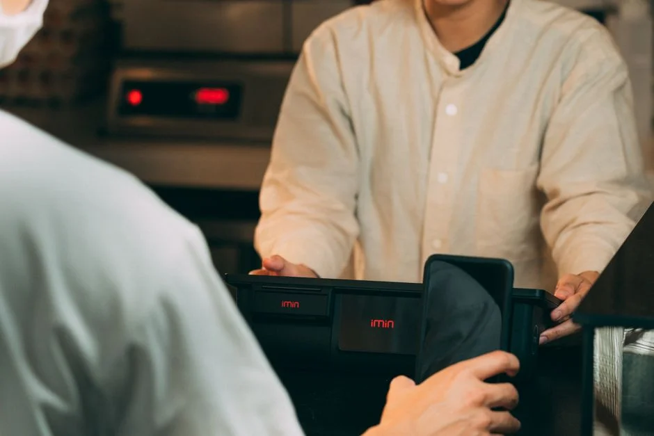 Persona sosteniendo un smartphone frente a una terminal de pago