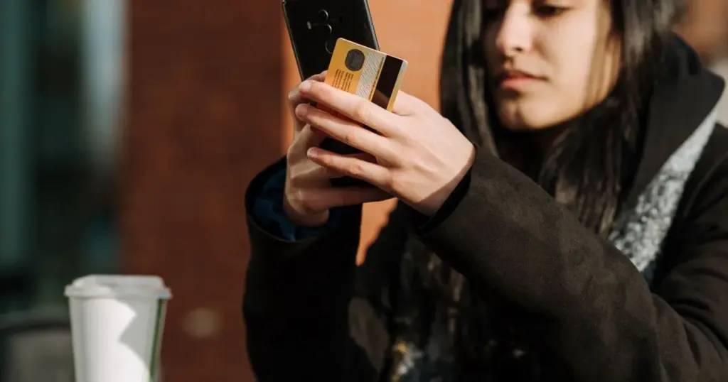 Mujer usando su celular con una tarjeta bancaria en la mano