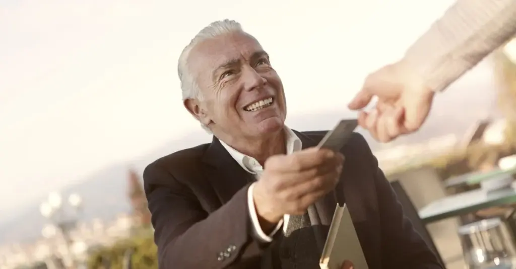 Hombre mayor sonriendo mientras entrega una tarjeta de crédito