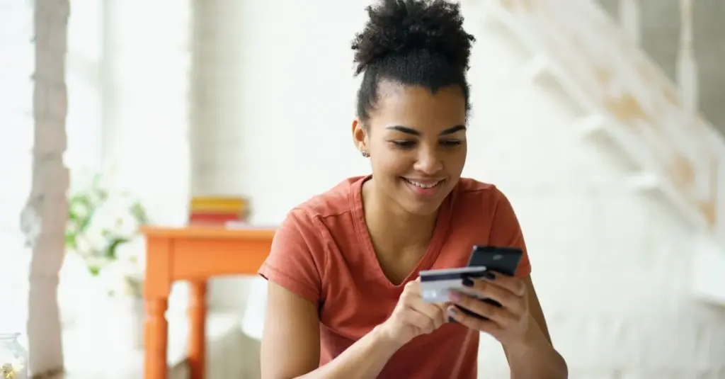 Joven sonriente comprando en línea con tarjeta y celular