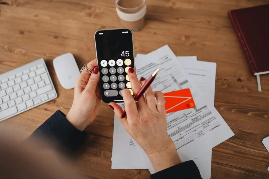 Mujer usando calculadora en el celular junto a documentos financieros