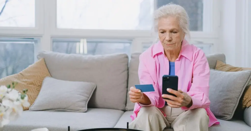 Mujer mayor revisando su tarjeta y su celular en casa