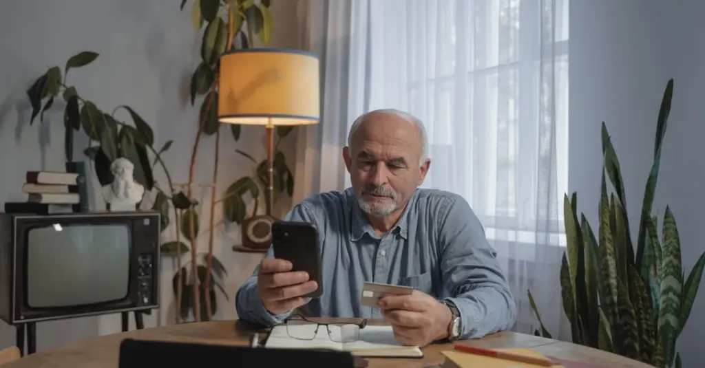 Hombre mayor sentado con smartphone y tarjeta de crédito