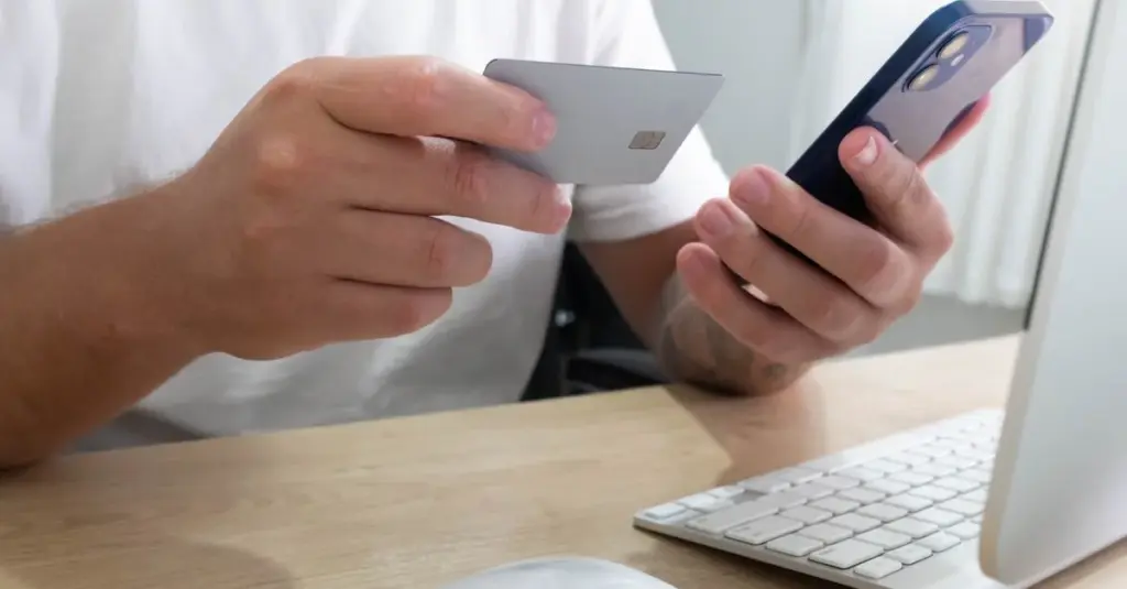 Persona sosteniendo una tarjeta de crédito y su celular para una compra en línea