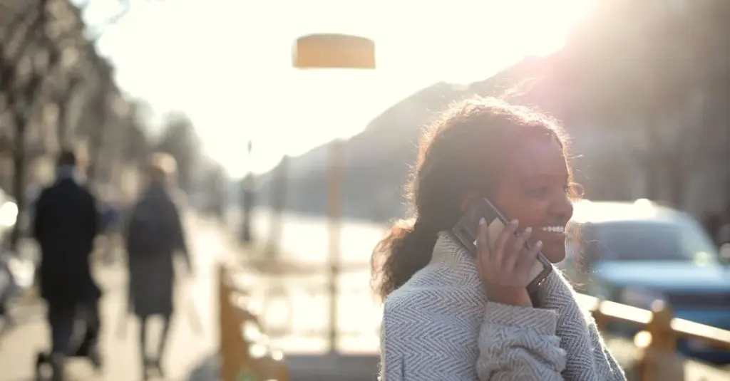 Mujer joven sonriendo mientras usa su celular al aire libre