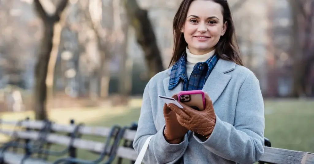 Mujer joven sonriendo con celular y tarjeta en un parque