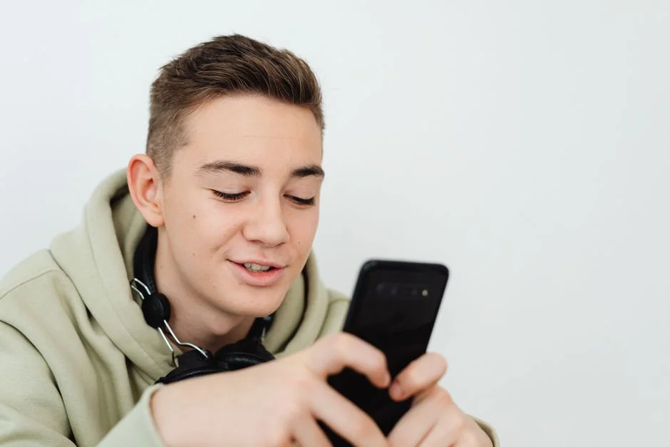 Joven sonriendo mientras usa el celular con audífonos al cuello