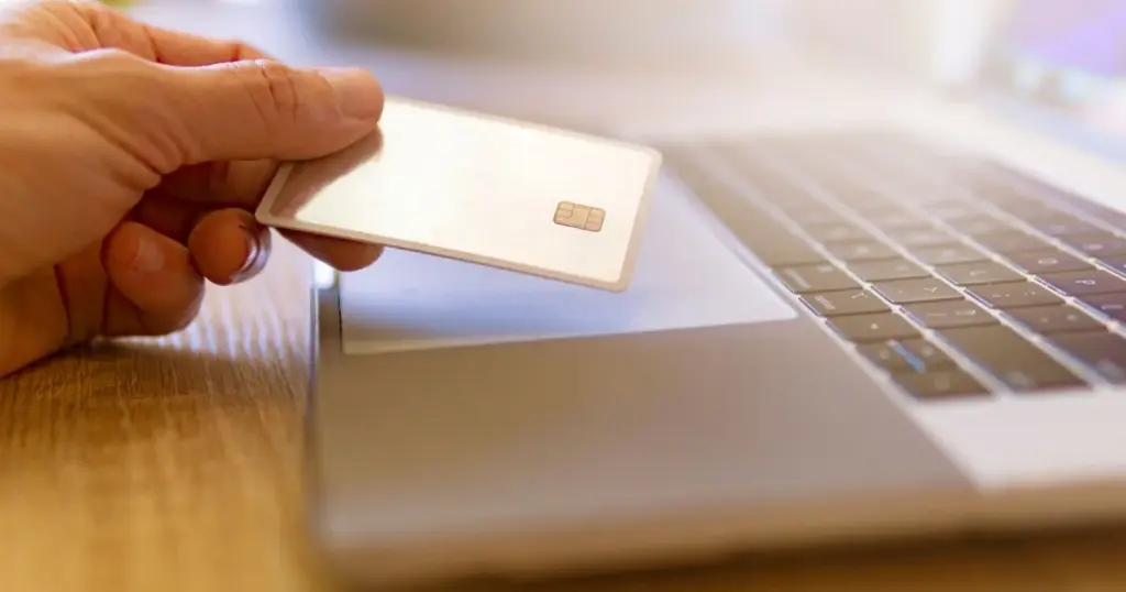 Persona sosteniendo una tarjeta de crédito junto a una laptop