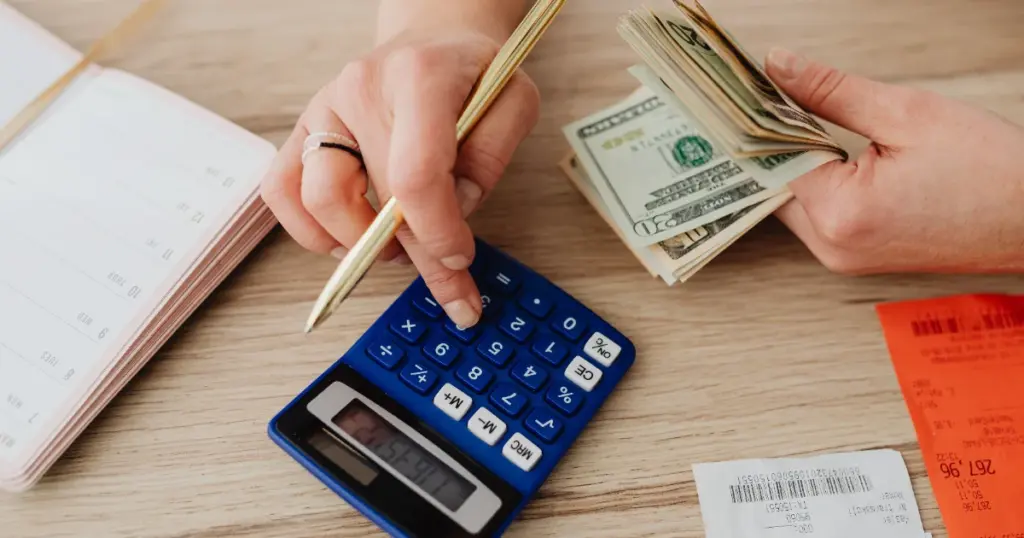 Manos calculando gastos con calculadora, dinero y recibos, representando la organización de un presupuesto familiar