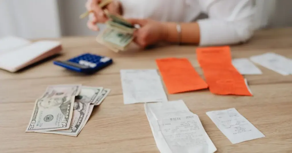 Persona contando billetes y recibos sobre una mesa, pagando una deuda