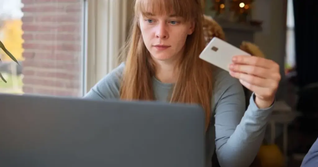 Mujer mirando una tarjeta genérica frente a su laptop, confundida por una negativa de crédito