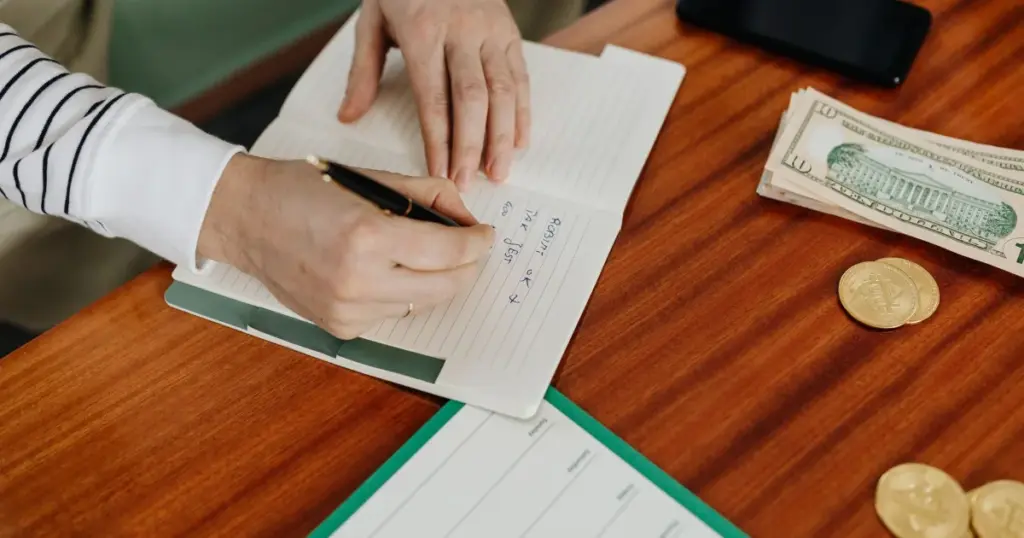 Persona anotando en un cuaderno junto a dinero en efectivo y su celular