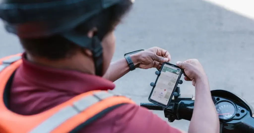 Conductor de aplicativo revisando el mapa en su celular montado en la moto