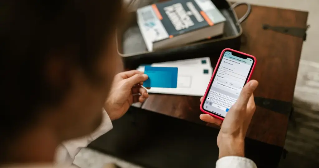 Persona sosteniendo una tarjeta y usando una app bancaria en el celular
