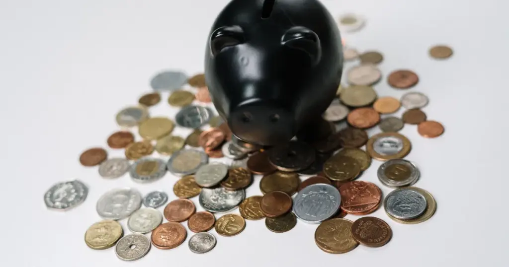 Alcancía negra rodeada de monedas sobre superficie blanca, simbolizando ahorro