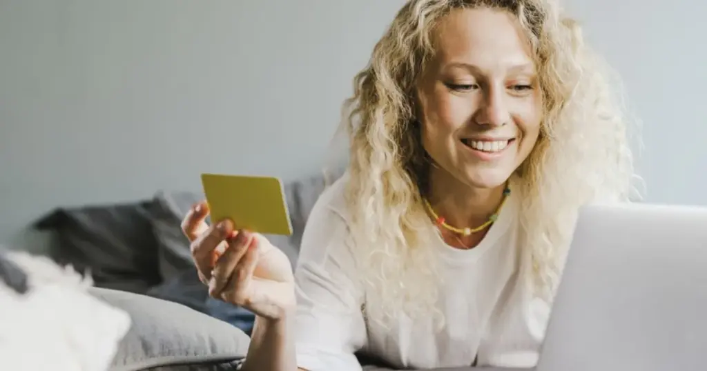 Mujer sonriente sosteniendo una tarjeta débito frente a la laptop