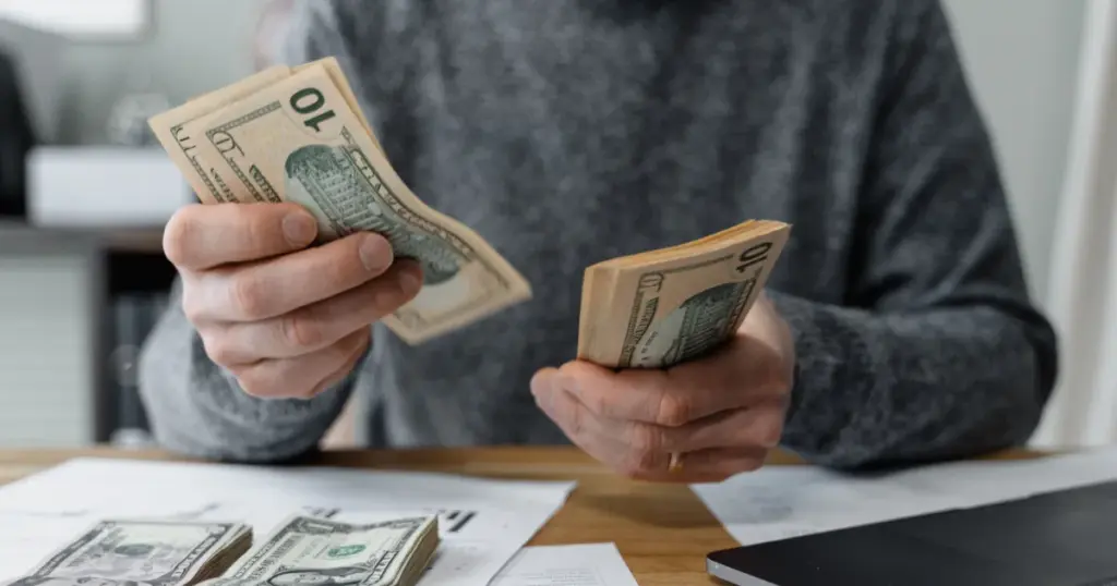 Persona contando efectivo con calculadora y papeles en el escritorio