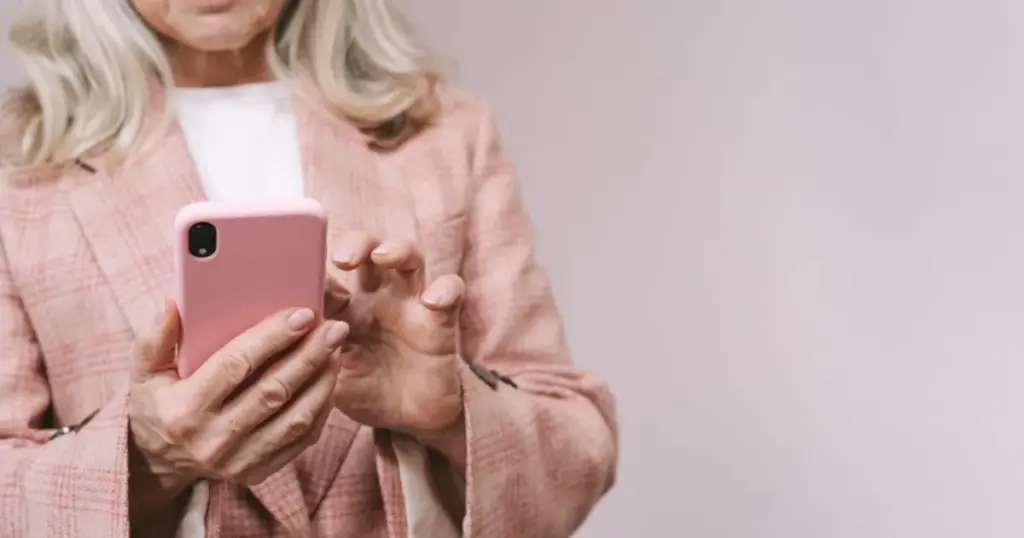 Mujer mayor sonriendo mientras usa el celular con estuche rosado
