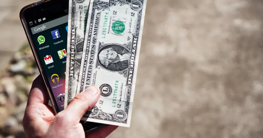 Mano sosteniendo billetes de dólares y un teléfono, remesas familiares