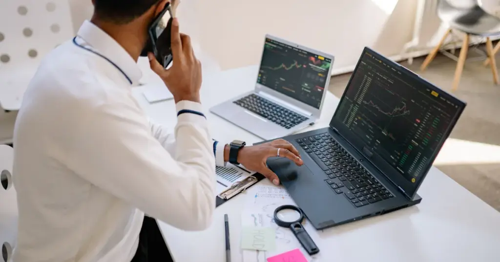 Hombre con celular trabajando en laptops con gráficos financieros