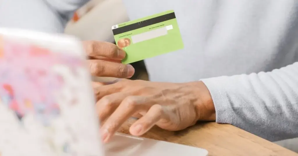 Manos sosteniendo tarjeta para compra online con laptop