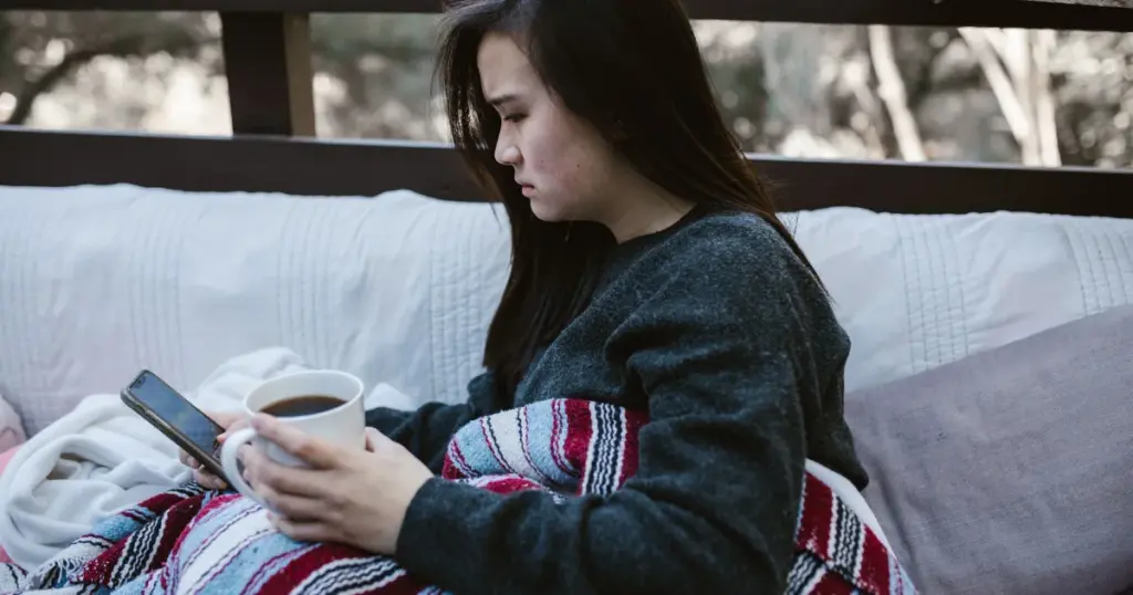 Mujer preocupada revisando el celular envuelta en una manta